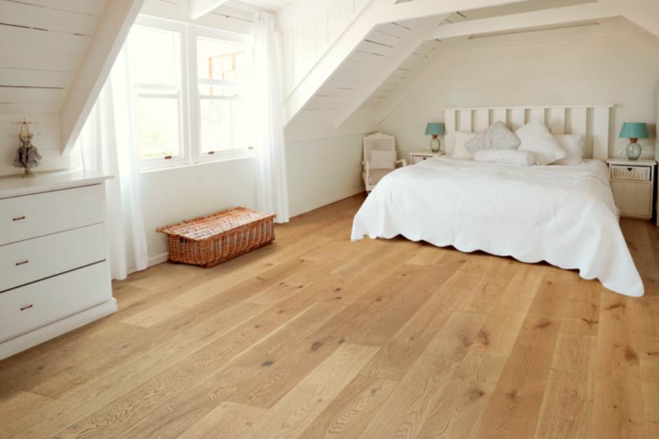 light hardwood flooring in bedroom with white bedding and white walls.